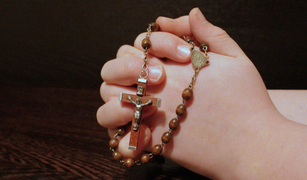 Hands clasped around a wooden rosary in prayer