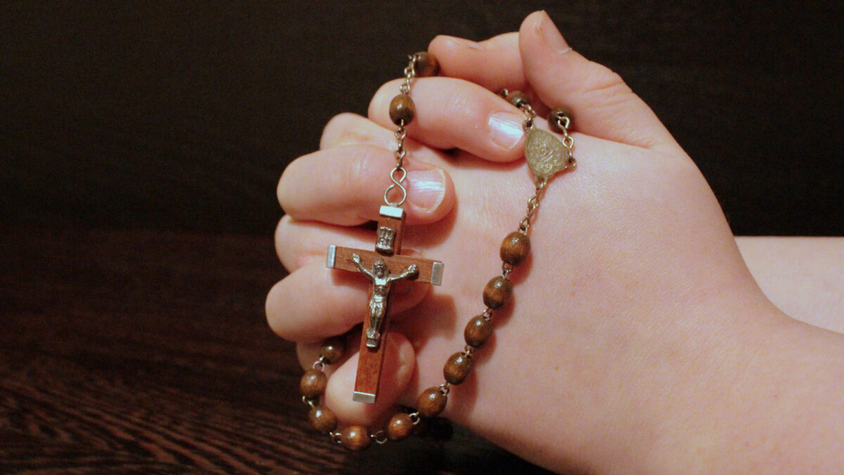 Hands clasped around a wooden rosary in prayer